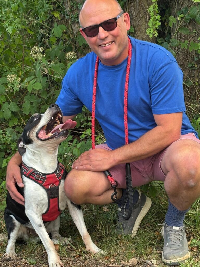 Jon smiling at camera when out with his dog in the woods.